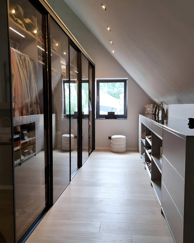 Modernes begehbarer Kleiderschrank bestehend aus einem Glaskleiderschrank und einer großzügigen Kommode unter der Dachschräge